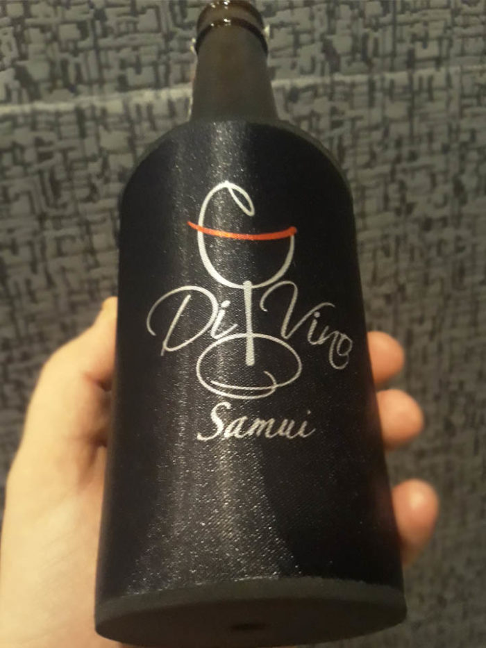 black shiny bottle cooler in hand. Bottle cooler have printed Divino Restaurant Logo